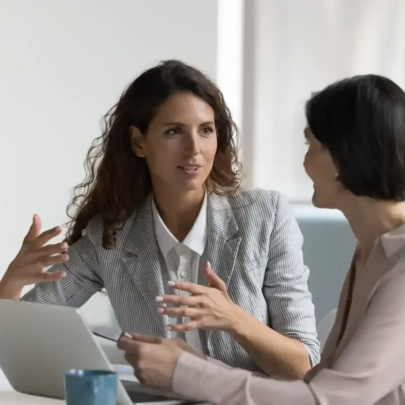 SEO specialist discussing with client the importance of keyword research in office in front of open laptop and coffee mug.