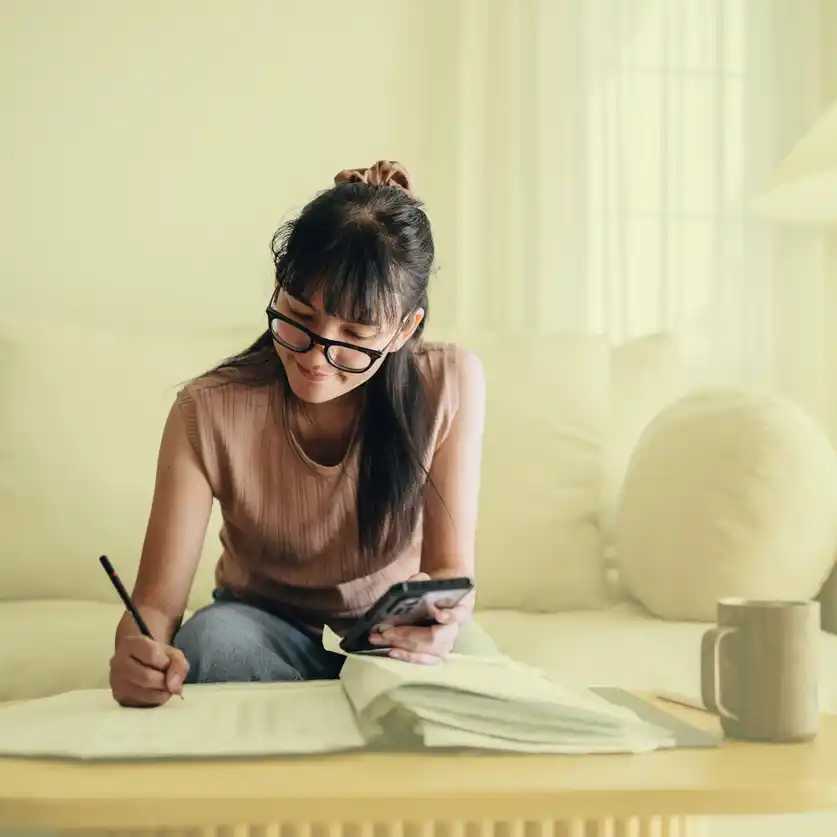 content strategy australia.jpg Modern woman with glasses and phone in hand writing into booklet.