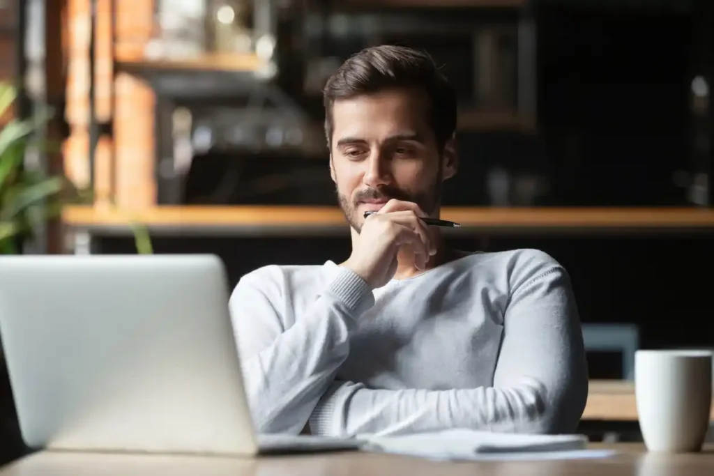 a financial copywriter sitting at a table with a laptop with his hand to his chin
