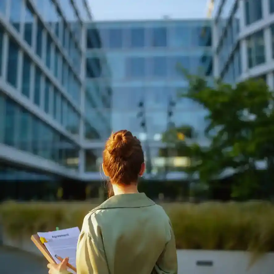 Mortgage broker looking at buildings with clipboard in hand.