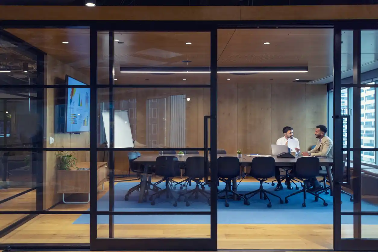 financial services copywriting and content marketing Two financial copywriters in business setting discussing across boardroom table behind glass doors.