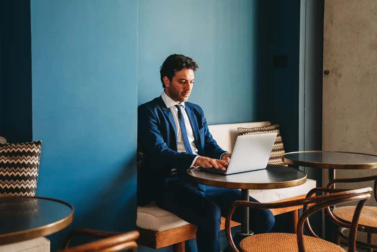 website content writing financial firms Savvy mortgage broker looking at website content in cafe with blue feature wall behind and empty seats around him.