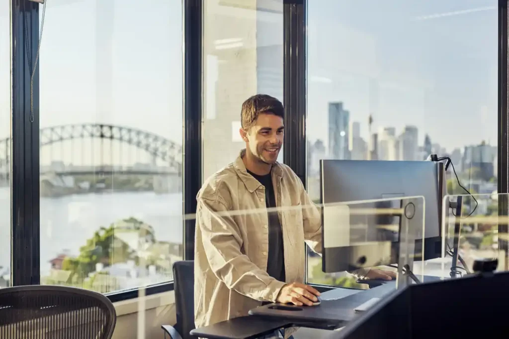 a male mortgage broker standing in front of a computer with Sydney Harbour Bridge in background