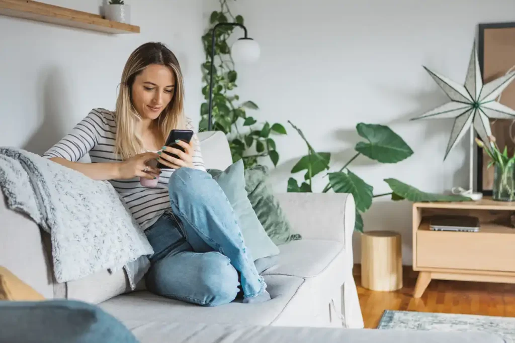 Female customer on couch at home searching for mortgage broker on phone. 